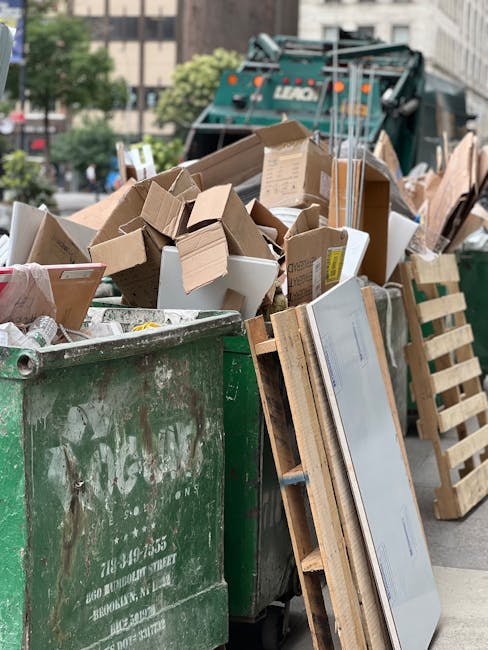 A large green waste collection skip filled with mixed rubbish, including numerous cardboard boxes, some flattened and others partially assembled, alongside a few white plastic containers and packing m